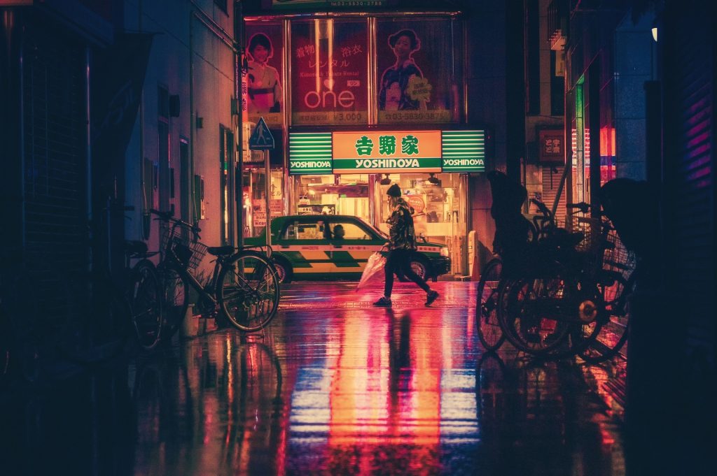 A woman walking on a Kyoto street at night, neon reflecting off the damp street surface.