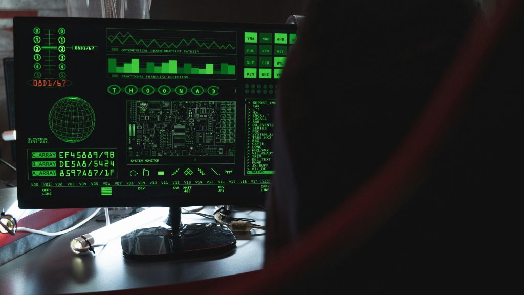 An over the shoulder shot of a hacker's computer screen, showing space-age schematics, hardware notes, and a console line in bright green against a black background.